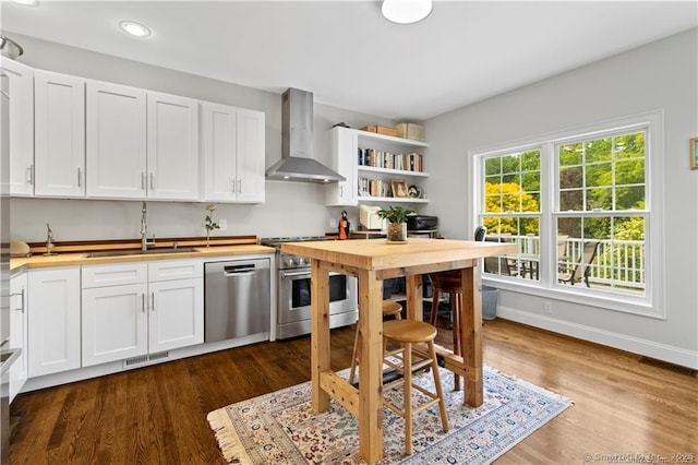 kitchen featuring dark wood-type flooring, white cabinets, wall chimney range hood, sink, and stainless steel appliances