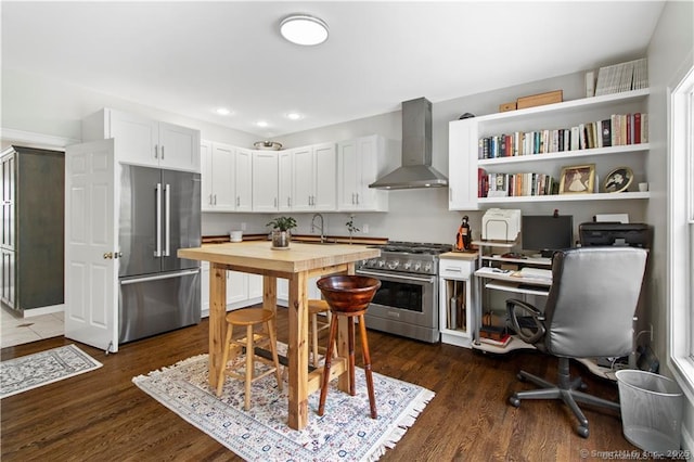 kitchen with sink, dark wood-type flooring, wall chimney range hood, high quality appliances, and white cabinets