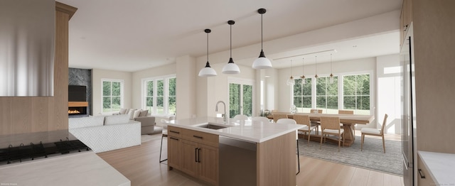 kitchen with dishwasher, a kitchen island with sink, sink, decorative light fixtures, and a large fireplace