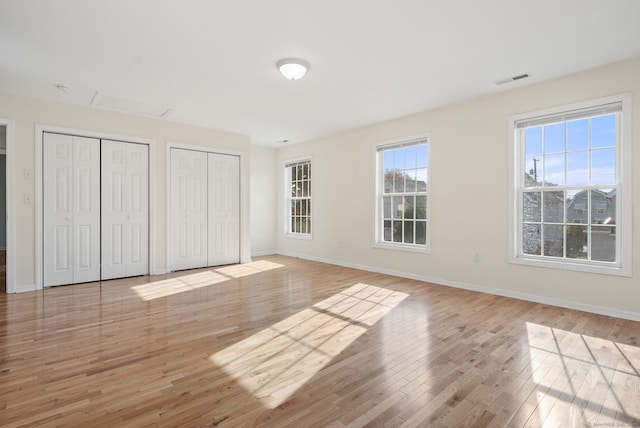 unfurnished bedroom with light hardwood / wood-style flooring and two closets