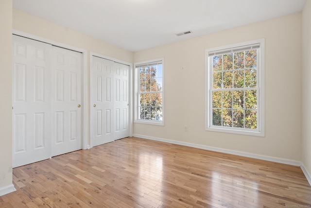 unfurnished bedroom featuring two closets, light hardwood / wood-style flooring, and multiple windows