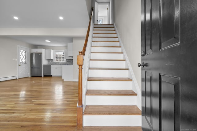 stairway with sink, hardwood / wood-style flooring, and baseboard heating