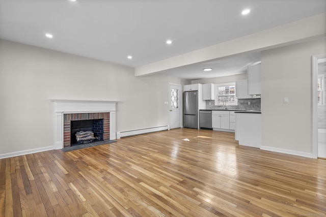 unfurnished living room featuring light hardwood / wood-style floors, baseboard heating, sink, and a fireplace