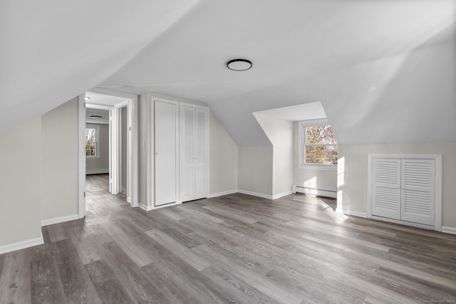 bonus room featuring a healthy amount of sunlight, light wood-type flooring, vaulted ceiling, and a baseboard heating unit