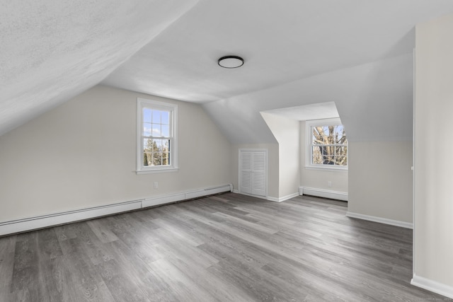 additional living space featuring a baseboard heating unit, a textured ceiling, vaulted ceiling, and light hardwood / wood-style flooring