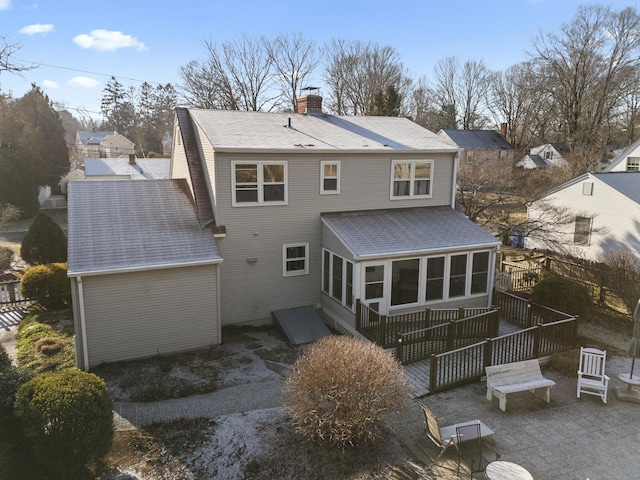 back of property with a wooden deck, a patio, and a sunroom