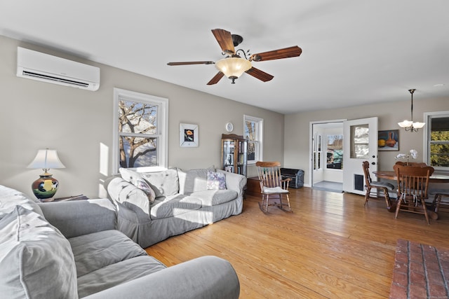 living room with light wood-type flooring, ceiling fan with notable chandelier, and a wall unit AC