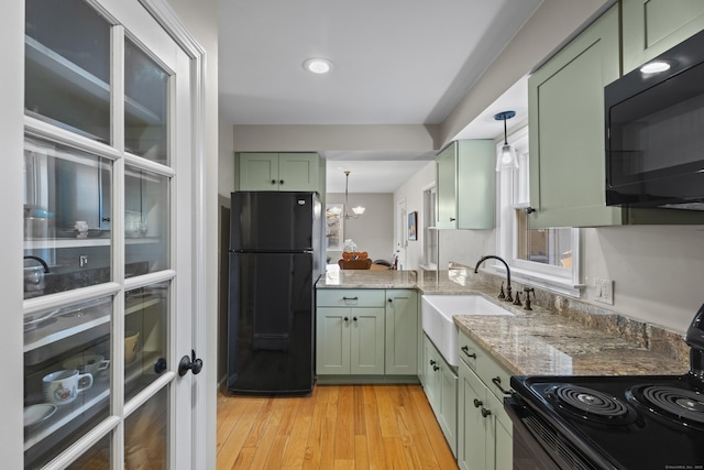 kitchen featuring black appliances, green cabinetry, pendant lighting, light stone counters, and sink