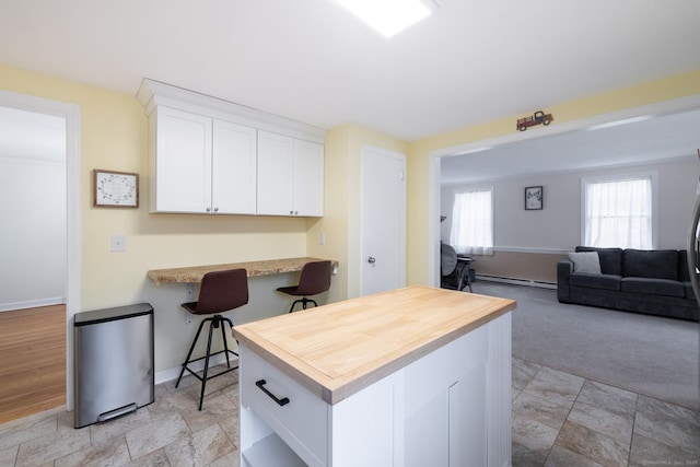 kitchen with a breakfast bar, white cabinetry, light carpet, and a baseboard heating unit