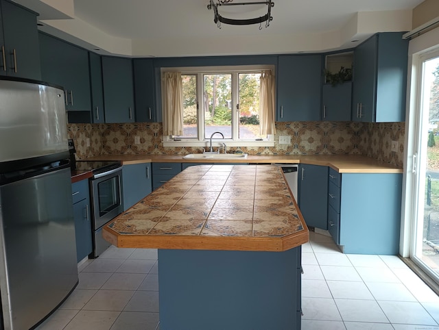 kitchen with blue cabinetry, sink, stainless steel appliances, tasteful backsplash, and light tile patterned floors