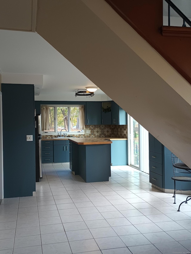 kitchen with wood counters, backsplash, sink, stainless steel refrigerator, and light tile patterned flooring