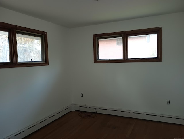 empty room featuring dark hardwood / wood-style flooring, a wealth of natural light, and a baseboard heating unit