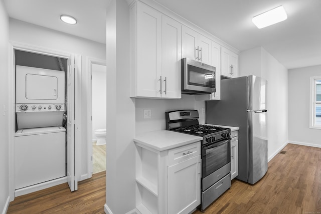 kitchen featuring dark wood-type flooring, stainless steel appliances, light stone counters, stacked washer / dryer, and white cabinets