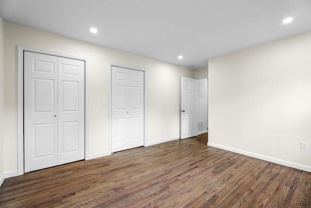 unfurnished bedroom featuring multiple closets and dark hardwood / wood-style flooring