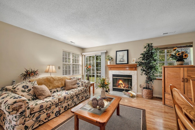 living room featuring a tiled fireplace, light hardwood / wood-style flooring, a healthy amount of sunlight, and a textured ceiling