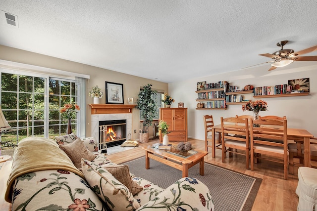 living room featuring a tile fireplace, a textured ceiling, hardwood / wood-style flooring, and ceiling fan