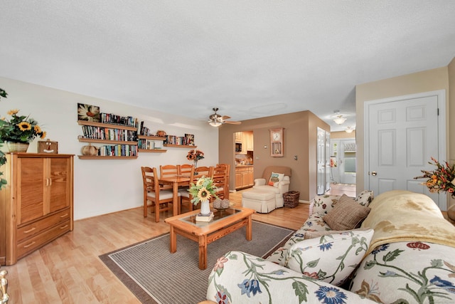 living room with ceiling fan, a textured ceiling, and light hardwood / wood-style flooring