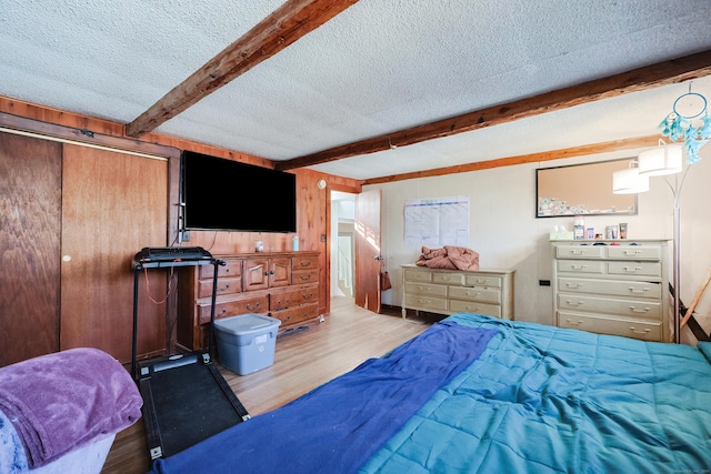 bedroom featuring a textured ceiling, beam ceiling, light hardwood / wood-style flooring, a closet, and wood walls