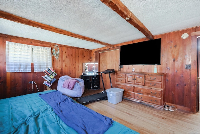 bedroom with beam ceiling, wood walls, light hardwood / wood-style floors, and a textured ceiling