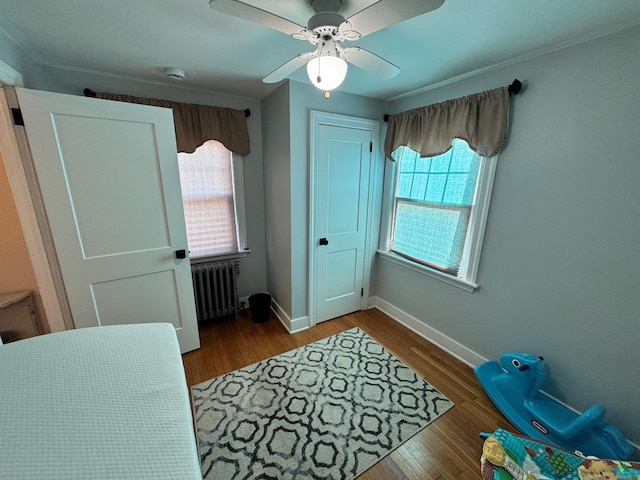 bedroom featuring wood-type flooring, multiple windows, radiator heating unit, and ceiling fan