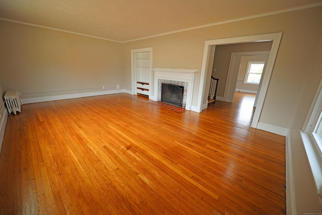 unfurnished living room featuring radiator heating unit, light hardwood / wood-style flooring, a brick fireplace, and ornamental molding