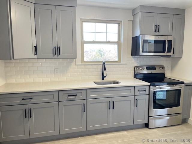 kitchen with appliances with stainless steel finishes, backsplash, gray cabinets, and sink