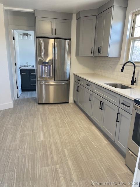 kitchen featuring sink, stainless steel fridge, gray cabinets, decorative backsplash, and range