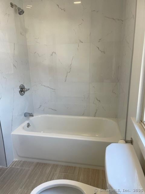 bathroom featuring tiled shower / bath combo and toilet