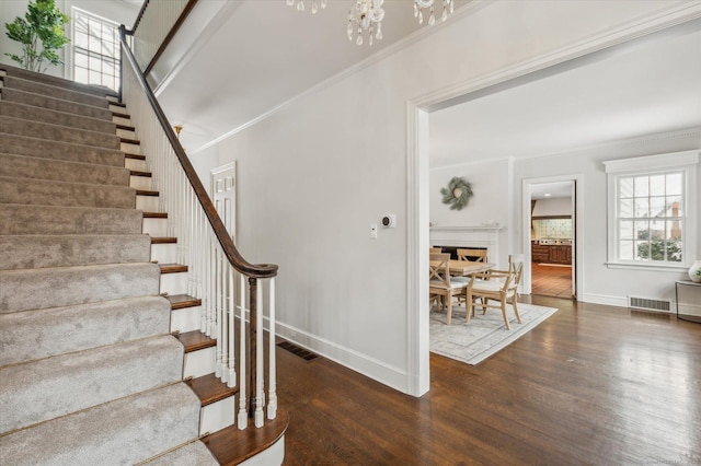 stairway with crown molding, an inviting chandelier, and wood-type flooring