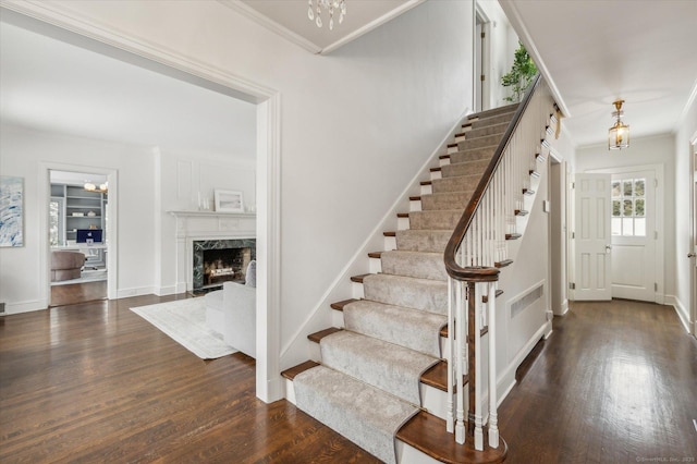 staircase with a chandelier, ornamental molding, a fireplace, and wood-type flooring