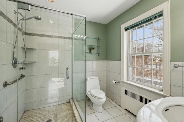 bathroom with radiator, tile patterned flooring, a shower with shower door, and tile walls