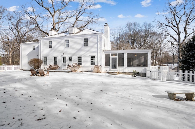 snow covered rear of property with a sunroom