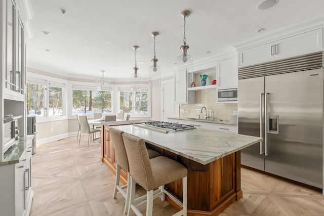 kitchen with built in appliances, light stone countertops, white cabinetry, a kitchen island, and decorative light fixtures