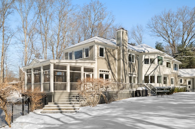 snow covered rear of property with a sunroom