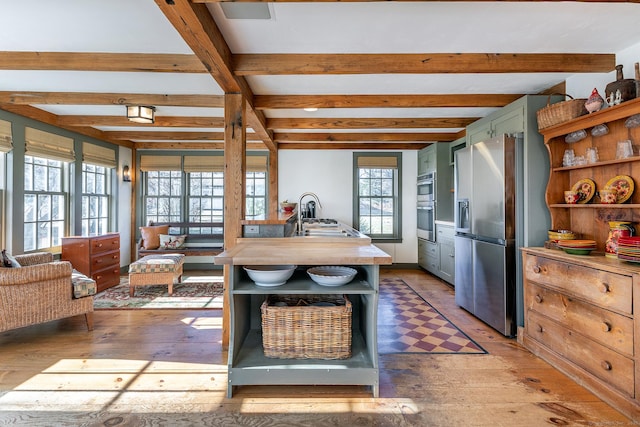 kitchen featuring appliances with stainless steel finishes, sink, beam ceiling, light hardwood / wood-style flooring, and green cabinets