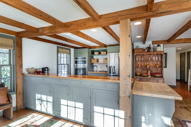 kitchen with kitchen peninsula, beam ceiling, light wood-type flooring, and stainless steel appliances