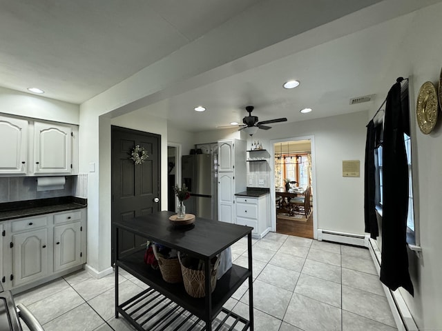 kitchen with stainless steel refrigerator with ice dispenser, a baseboard heating unit, light tile patterned floors, and white cabinets