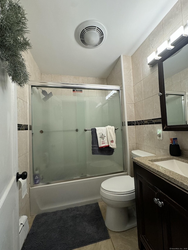 full bathroom featuring toilet, combined bath / shower with glass door, tile walls, baseboard heating, and vanity