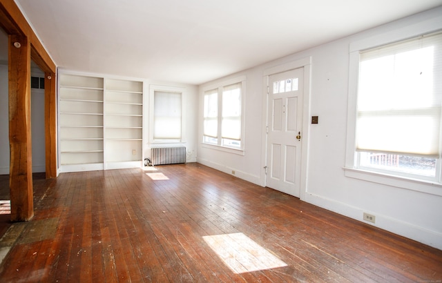 unfurnished living room with dark hardwood / wood-style floors, built in features, radiator heating unit, and a wealth of natural light