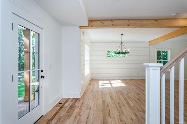 doorway to outside featuring an inviting chandelier, wooden walls, beam ceiling, and light hardwood / wood-style floors