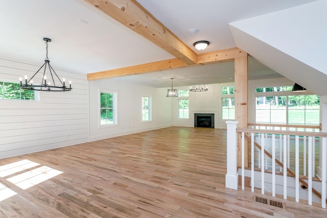 unfurnished living room with light wood-type flooring, wooden walls, a notable chandelier, and beam ceiling