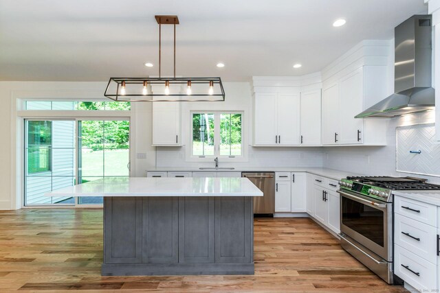 kitchen featuring wall chimney exhaust hood, white cabinetry, decorative light fixtures, a kitchen island, and stainless steel appliances