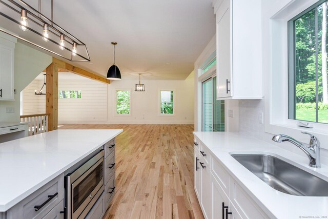 kitchen featuring white cabinetry, stainless steel microwave, sink, and hanging light fixtures