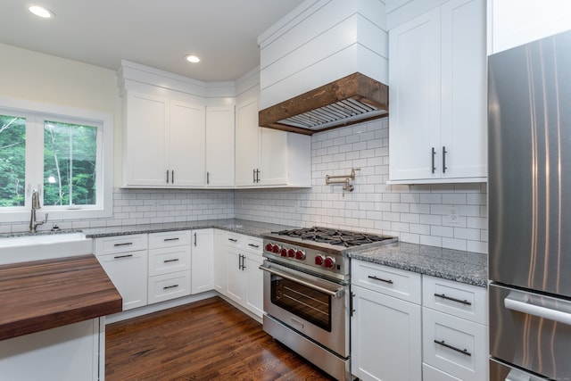 kitchen with premium range hood, white cabinetry, backsplash, dark stone counters, and stainless steel appliances