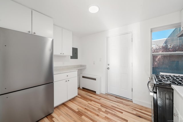 kitchen featuring electric panel, radiator heating unit, light wood-type flooring, appliances with stainless steel finishes, and white cabinetry