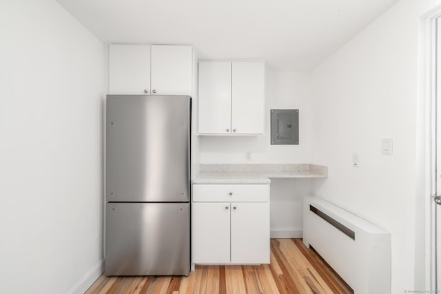 kitchen featuring stainless steel refrigerator, white cabinetry, radiator heating unit, electric panel, and light wood-type flooring