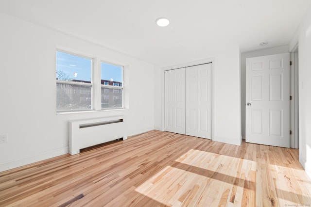 unfurnished bedroom featuring light wood-type flooring, radiator heating unit, and a closet