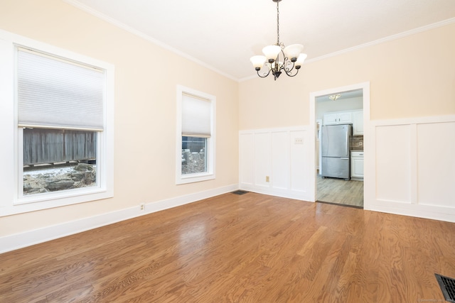 spare room with wood-type flooring, an inviting chandelier, and ornamental molding