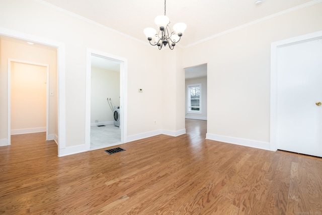 unfurnished dining area with hardwood / wood-style flooring, washer / dryer, crown molding, and an inviting chandelier