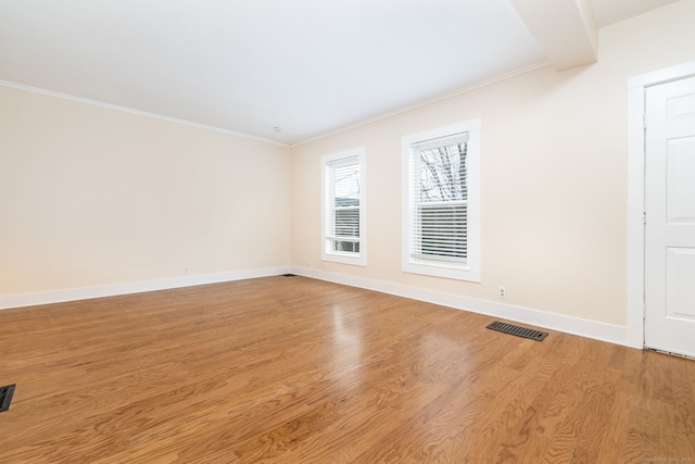 empty room with ornamental molding, light hardwood / wood-style flooring, and beamed ceiling